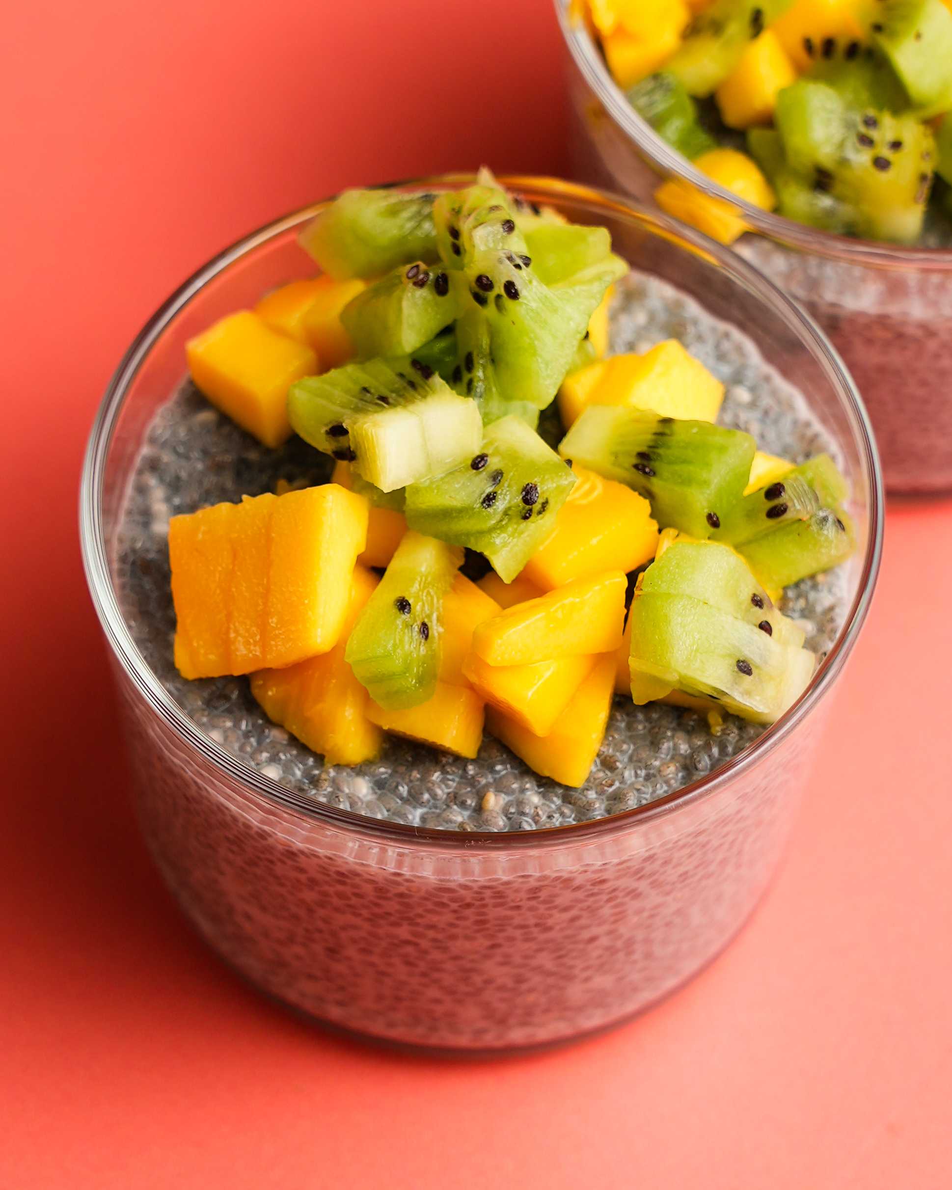 Two chia seed puddings with mango and kiwi on top sit in the front of the image, with Califia Farms Unsweetened Almondmilk off to the side.