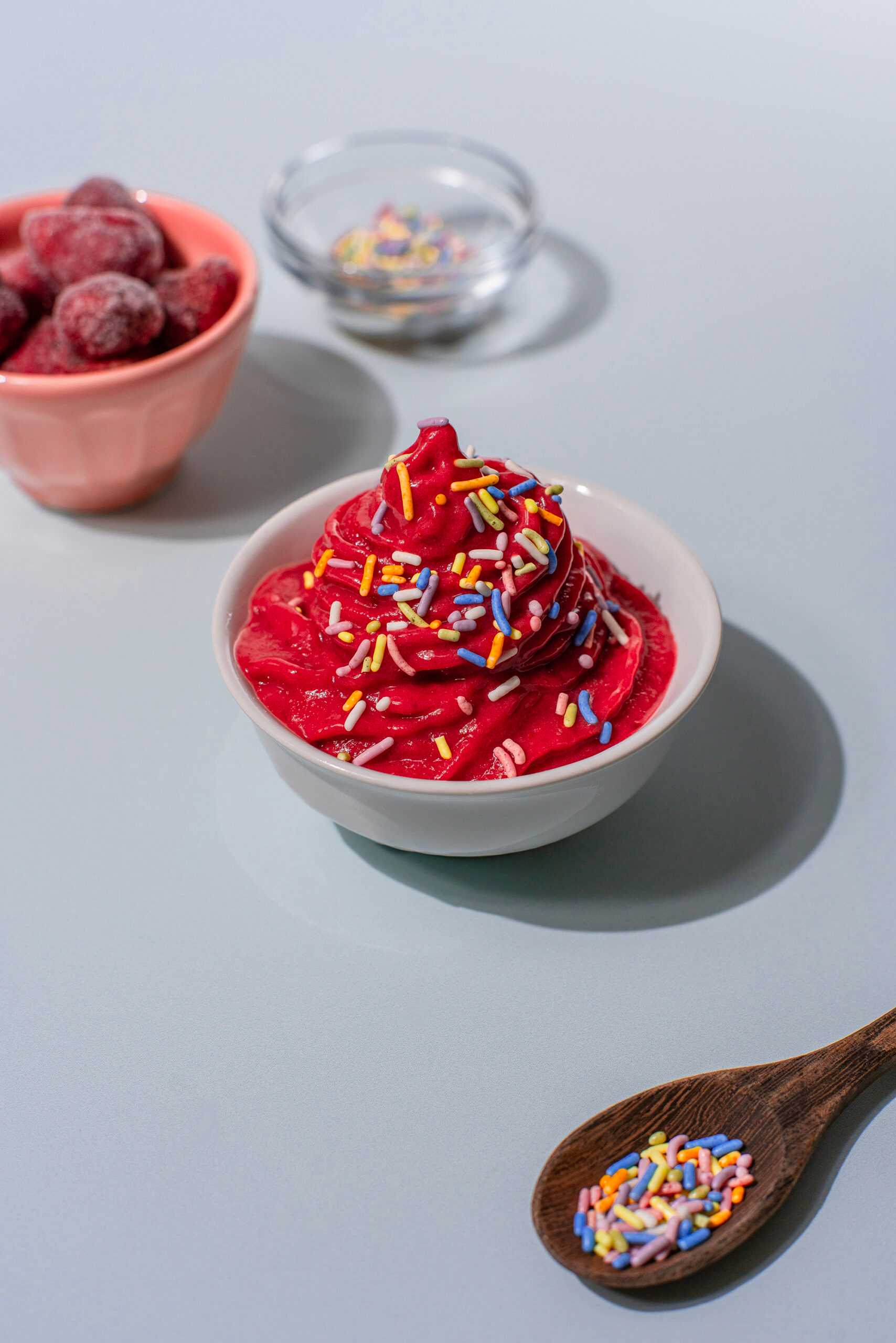 A bowl of strawberry soft serve sits in the center of the image, with rainbow sprinkles on top.