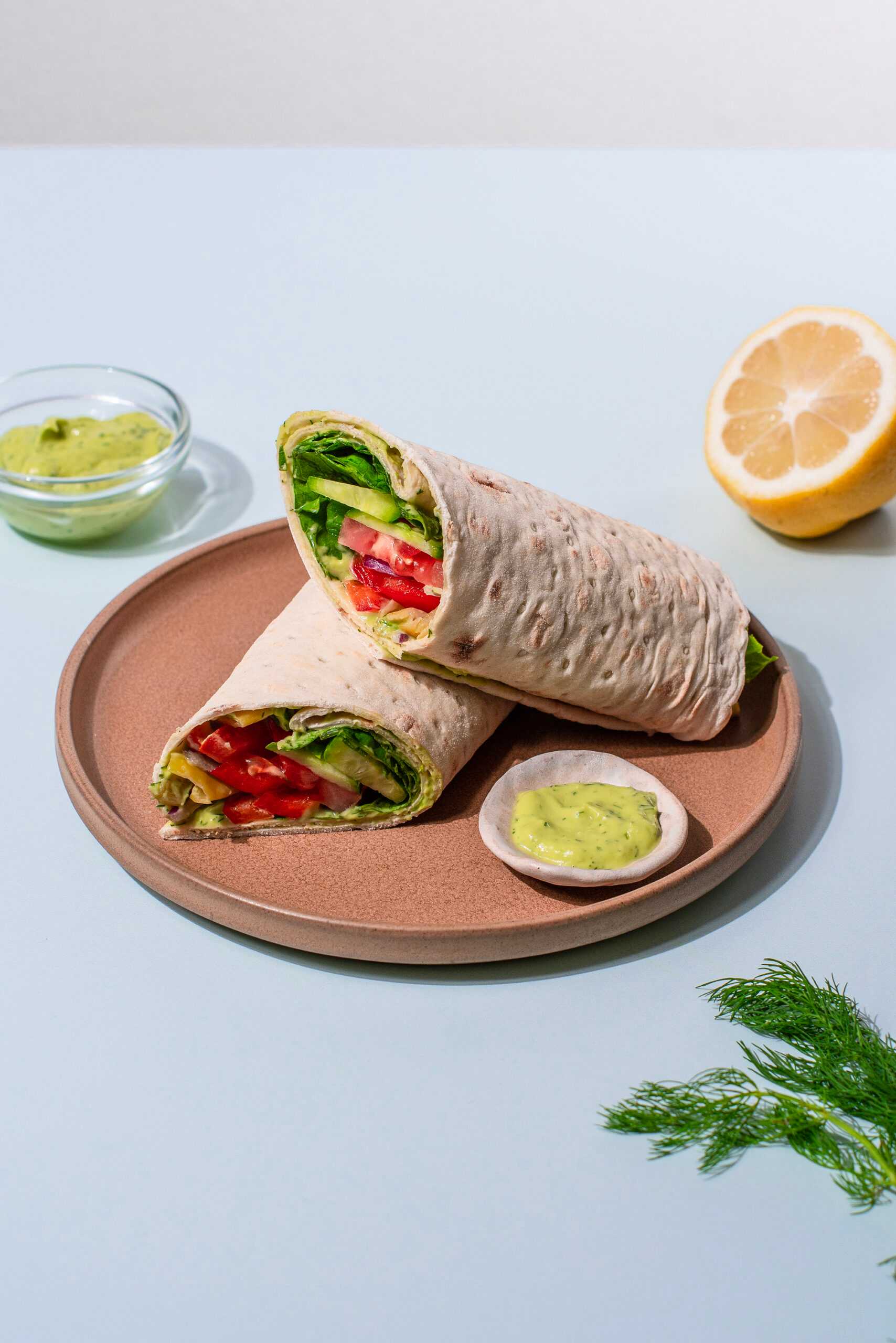 Veggie-filled wraps sit in the center of the image on a plate, surrounded by lemons and herbs.